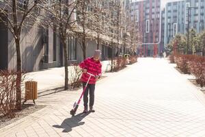 pequeño niña montando un scooter en el parque en un soleado primavera día. activo ocio y al aire libre deporte para niños foto