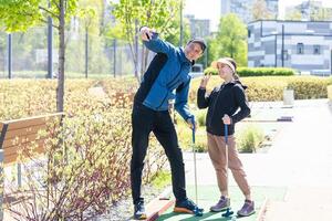 Sharing with golf experience. Cheerful young man teaching his daughter to play mini golf at the day time. Concept of friendly family photo