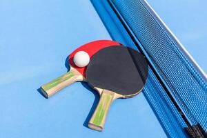 Two table tennis or ping pong rackets and ball on blue table with net photo