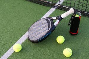 azul padel raqueta y amarillo pelotas metido en Corte cerca red en soleado día foto