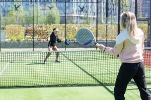 positive mother and daughter standing on court with padel rackets photo