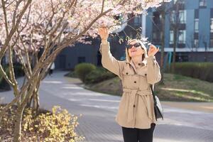 women is taking picture of blossoming cherry on mobile phone on street in spring photo