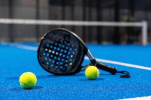 Kyiv, Ukraine, April 18, 2024. Black professional paddle tennis racket and ball with natural lighting on blue background. Horizontal sport theme poster, greeting cards, headers, website and app photo