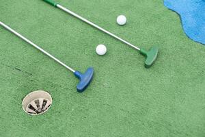 Mini-golf clubs and balls of different colors laid on artificial grass photo