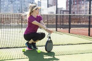 Young female smiling and looking at camera while playing padel against green background photo