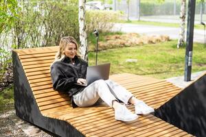 girl with a laptop on a bench in the park on a background of greenery photo