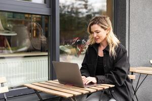 Businesswoman working with laptop in outdoor cafe. Corporate blog photo