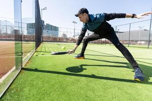 A padel player jump to the ball, good looking for posts and poster. Man with black racket playing a match in the open behind the net court outdoors. Professional sport concept with space for text photo