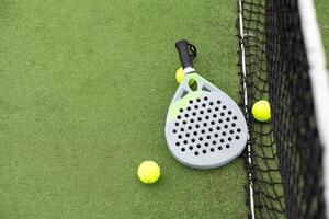 de cerca ver de un paleta raqueta y pelotas en un padel tenis Corte cerca el neto. verde antecedentes con blanco líneas. deporte, salud, juventud y ocio concepto. deportivo equipo. foto