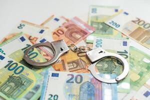 Police handcuffs lies on a set of green monetary denominations of 100 euros. A lot of money forms an infinite heap photo