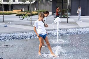 linda joven hermanas jugando en fuentes niños teniendo divertido con agua en soleado verano día. activo ocio para niños. foto