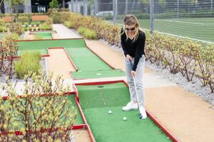 Woman playing mini golf and trying putting ball into hole. Summer leisure activity photo