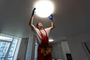 Electrician at work. Service for the repair of electrical wiring and replacement of ceiling lamps. A builder is installing a loft-style wooden ceiling. Rent-a-gent helps with the housework photo