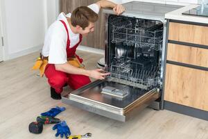 Repair of dishwashers. Repairman repairing dishwasher in kitchen photo