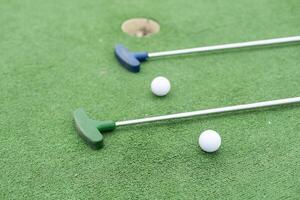 Mini-golf clubs and balls of different colors laid on artificial grass photo