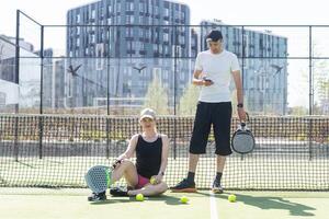 retrato de positivo joven mujer y adulto hombre en pie en padel tenis corte, participación raqueta y pelota, sonriente foto