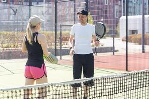 Portrait of positive young woman and adult man standing on padel tennis court, holding racket and ball, smiling photo