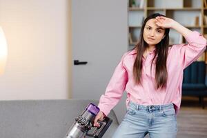 Tired and exhausted woman vacuuming house, cleaning rug carpet in living room, frustrated with doing much work about the house resting for a minute wiping forehead after finishing work, taking break. photo