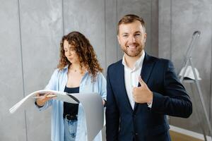 A young designer discusses the plans and design of the room with the customer. The customer is engrossed in work, looks into the camera and shows a thumbs up gesture. photo