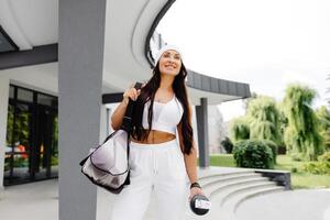 Beautiful woman ready to start her training. Energetic woman is going to gym with sports bag and bottle in hand photo