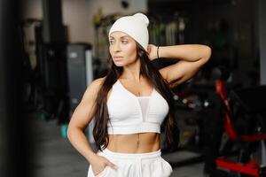 Beautiful fit woman looking at camera after gym exercise. Middle aged woman wearing sports bra and pants standing near simulator in gym photo