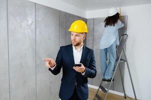 un joven empresario sostiene un teléfono en su manos y cheques el trabajo de un diseñador en creando un interior en un habitación. el concepto de reparar en un moderno diseño. foto