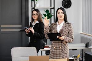 Two young attractive women are working in the office. A woman is talking on the phone, and her colleague is making notes in a notebook photo
