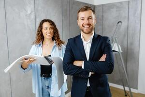 A young designer discusses the plans and design of the room with the customer. The customer is engrossed in work, looking at the camera with his arms crossed in front of him photo