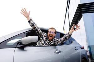 Excited young man showing a car key, sitting inside his new vehicle photo