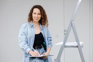 un joven bonito niña diseñador mantiene documentos mientras en pie a su lugar de trabajo. Departamento renovación y diseño concepto foto