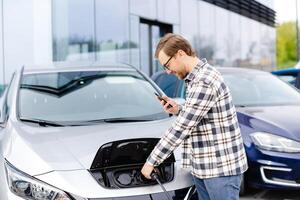 Young man plugging charging cable into the car socket. Electric car charging concept photo