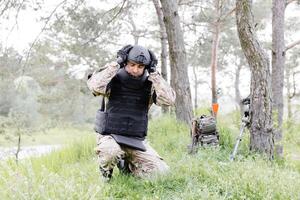 un hombre en un militar uniforme y un a prueba de balas chaleco trabajos en el bosque a desminar el territorio. un hombre pone en un protector casco antes de comenzando trabajo foto