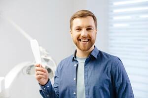 hermoso masculino paciente mirando a su hermosa sonrisa en pie a el dental oficina foto