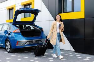 A young girl stopped to charge her electric car, and in the meantime goes to rest, carrying a suitcase photo