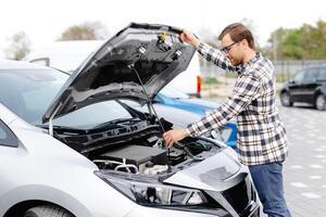 Young man checking under the hood of his car to figure out what the problem is. photo