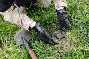 un hombre en un militar uniforme y un a prueba de balas chaleco trabajos en el bosque a desminar el territorio. un hombre desactiva un antipersonal mía foto