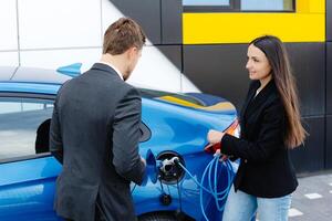 ventas gerente demostración cómo a cargar eléctrico coche a un joven cliente mujer, enchufar cable dentro el coche enchufe a el coche concesión al aire libre foto