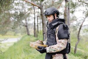 A man in a special suit works with a detector and found an explosive device. A man tries to neutralize an anti-tank mine photo