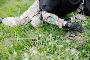 un hombre en un militar uniforme y un a prueba de balas chaleco trabajos en el bosque a desminar el territorio. un hombre advierte de peligro por haciendo un rojo marca foto