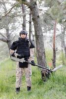 un hombre en un militar uniforme y a prueba de balas chaleco trabajos en el bosque con un metal detector. un dragaminas realiza trabajo en desminado el territorio foto