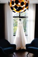 Wedding dress hanging on rack in front of window photo