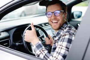 Man customer sitting in car salon and higgind the steering wheel, choosing auto and wanting to buy new automobile in showroom dealership store. Car sales concept photo