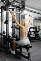 deportivo hembra mujer en gris traje tirado en Deportes simulador en gimnasia. espalda músculos son muy tenso. foto
