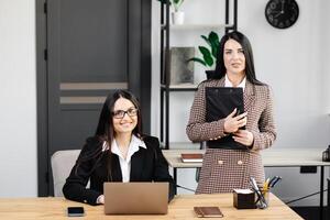 Two young attractive women are working in the office. Women working on a new project, doing work on a laptop. photo