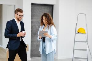 joven diseñador y cliente empresario son diseño interior en pie con digital tableta en el nuevo vivo habitación interior foto