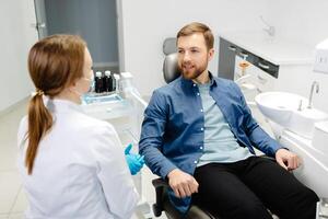 Blonde female dentist in dental office talking with male patient and preparing for treatment. Handsome bearded man in dentist chair looking at his doctor with smile photo
