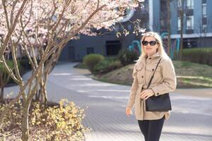 Blonde touches a branch of blooming cherry standing in the park photo