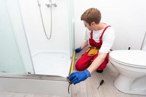 repairmen in uniform measuring modern shower cabin in bathroom photo