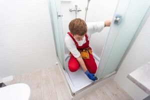 Plumber using silicone cartridge for fixing aluminum batten of shower cabin photo