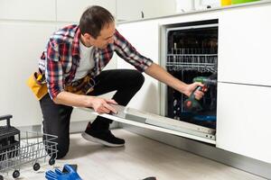 Professional worker repairing the dishwasher in the kitchen photo